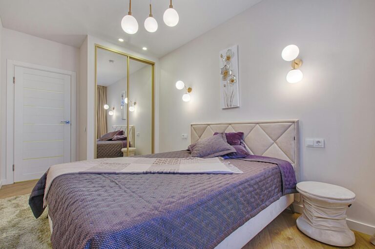 Elegant bedroom with purple decor, modern lighting, and mirror wardrobe.