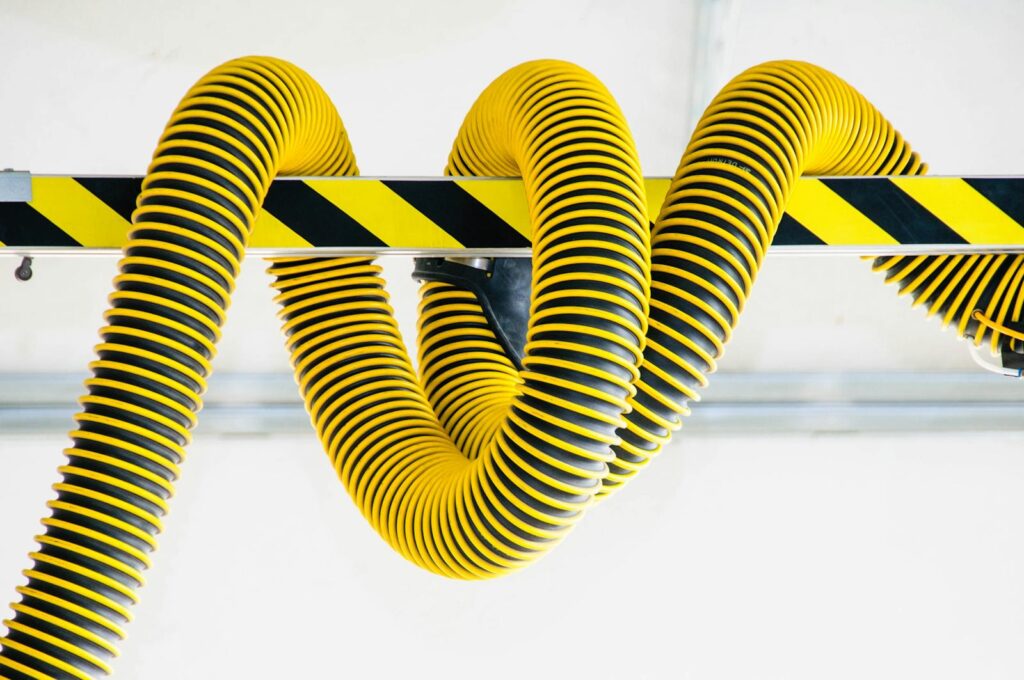 Close-up of yellow industrial hoses coiled around a safety-striped metal beam, showcasing modern industrial design.